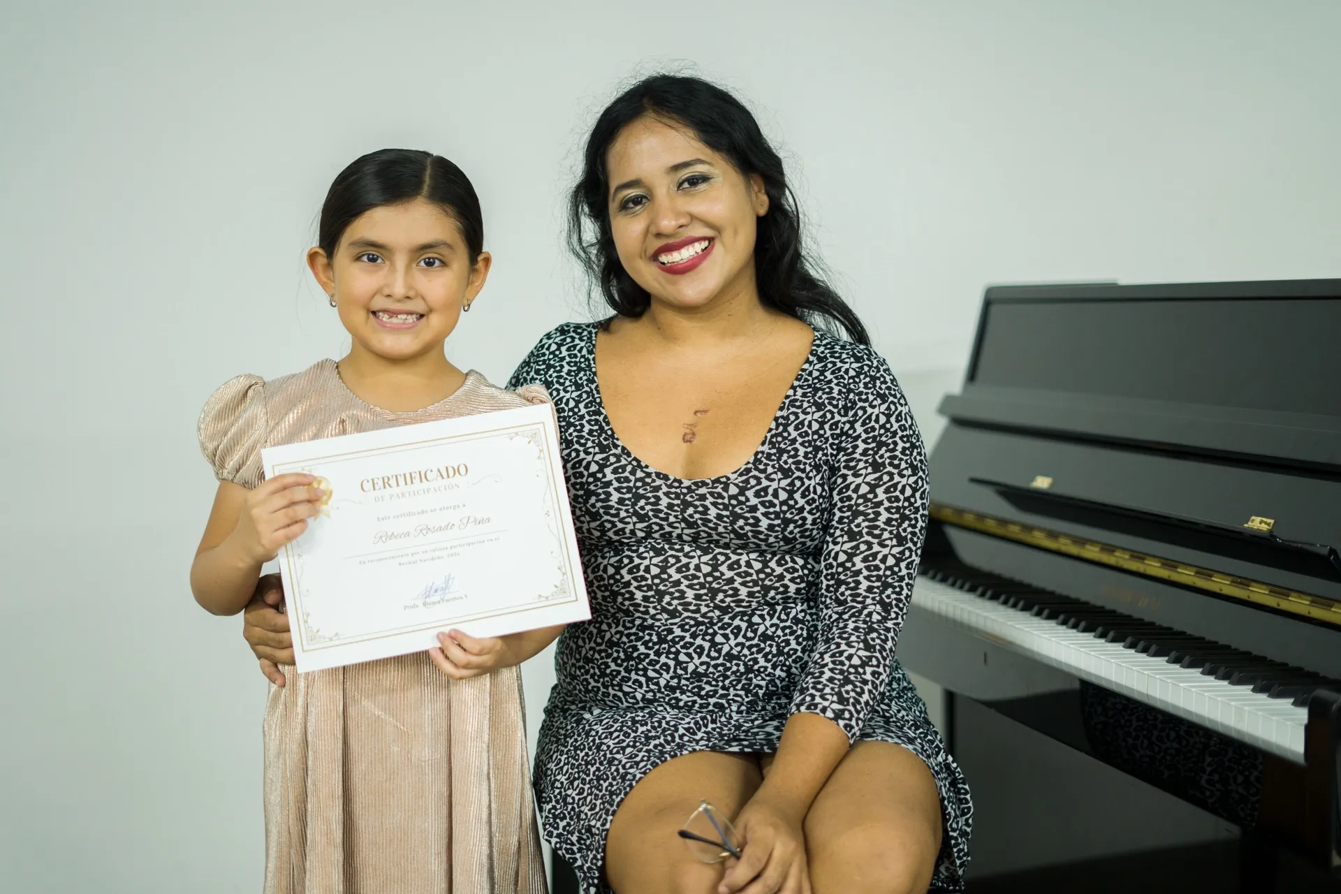 Una alumna muestra su certificado de participación junto a su maestra.