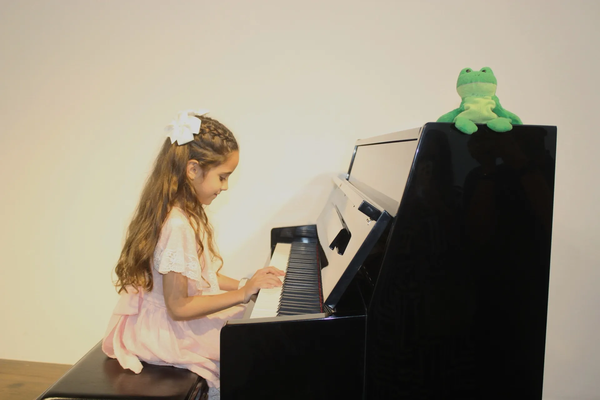 Una niña toca el piano con un peluche de rana sobre el instrumento.