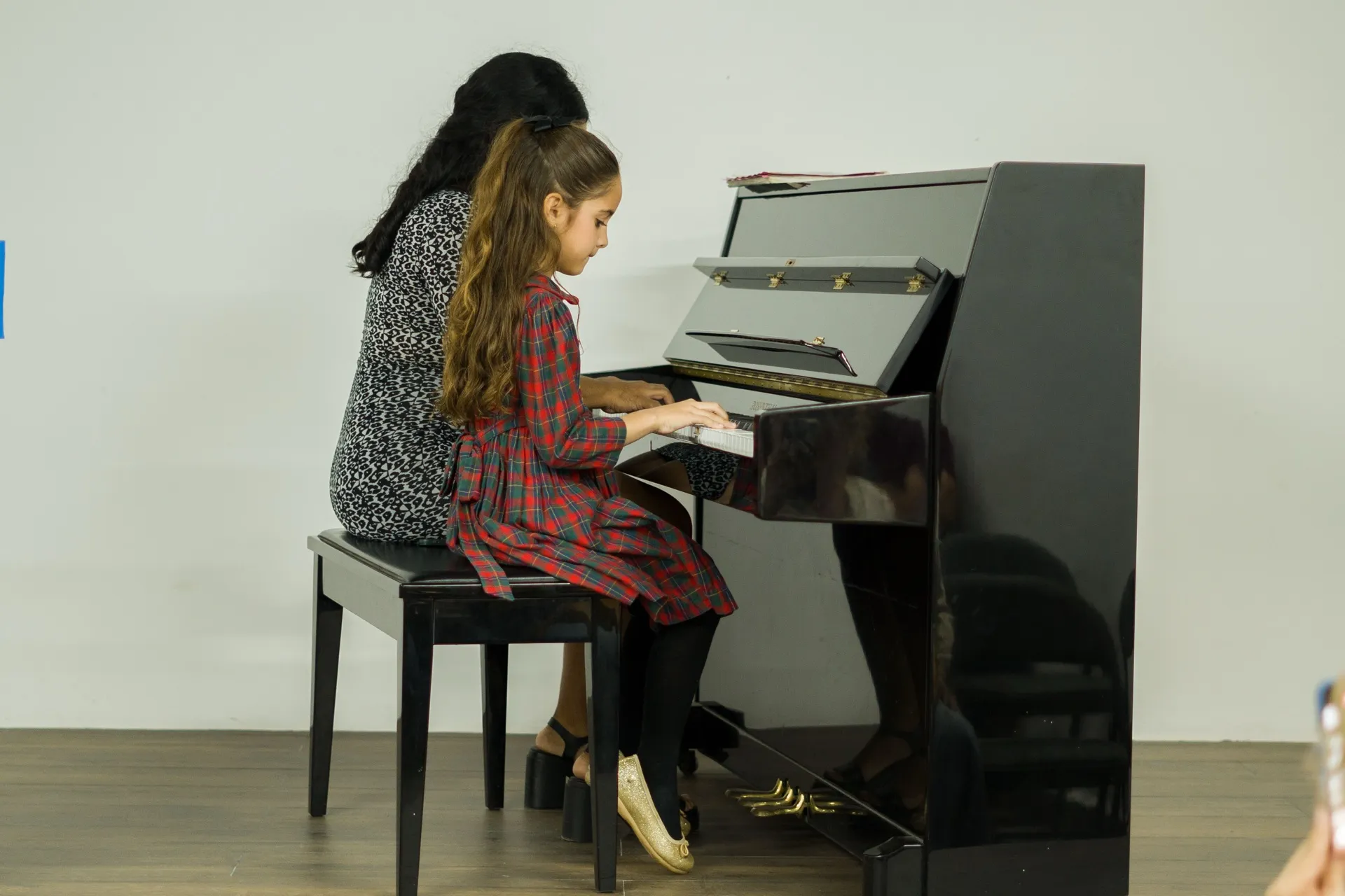 Una maestra acompaña a una niña en su clase de piano.
