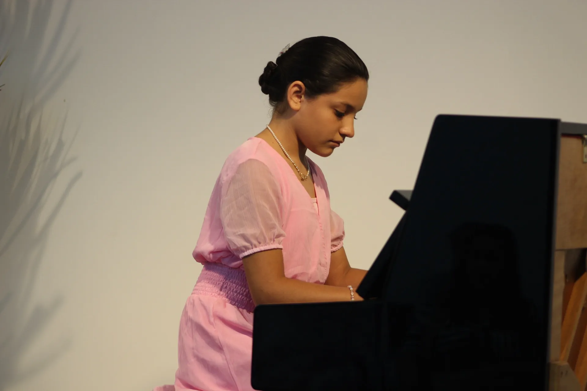 Una alumna con vestido rosa toca el piano, de perfil.